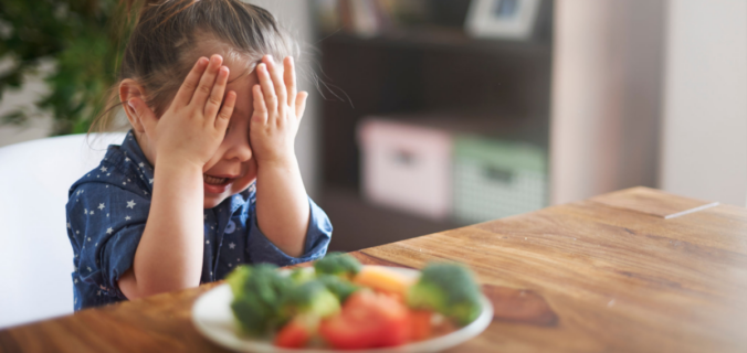 Criança brincando com um prato de alimentos orgânicos coloridos e nutritivos, descobrindo a diversão na alimentação saudável.