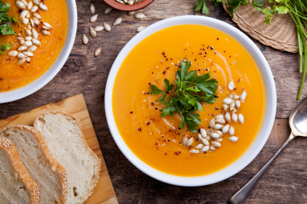 Foto de uma tigela fumegante de sopa de abóbora orgânica, decorada com uma pitada de ervas frescas. O vapor envolve o prato, transmitindo uma sensação de calor e sabor irresistível.