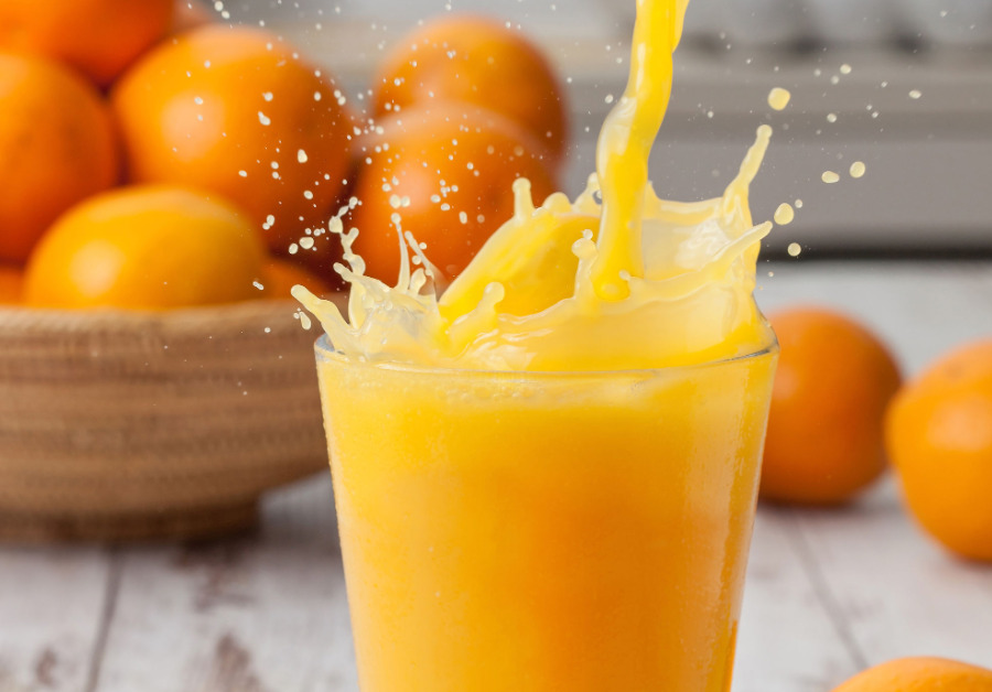 Copo de suco de laranja orgânico com gelo e uma fatia de laranja, indicando ser uma bebida refrescante e deliciosa.